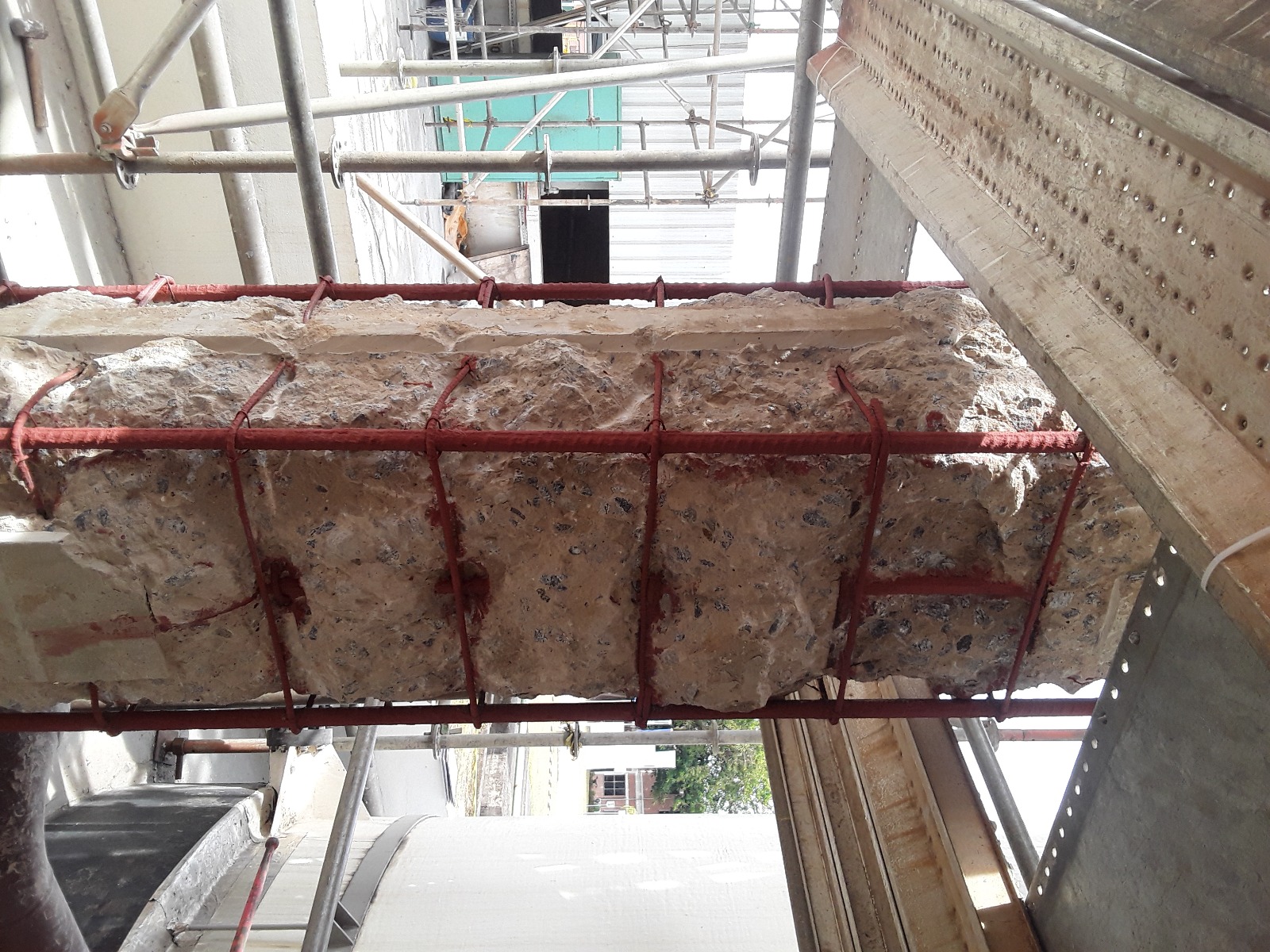 Detalhe de pilar com concreto removido localmente e armaduras aparentes com revestimento vermelho