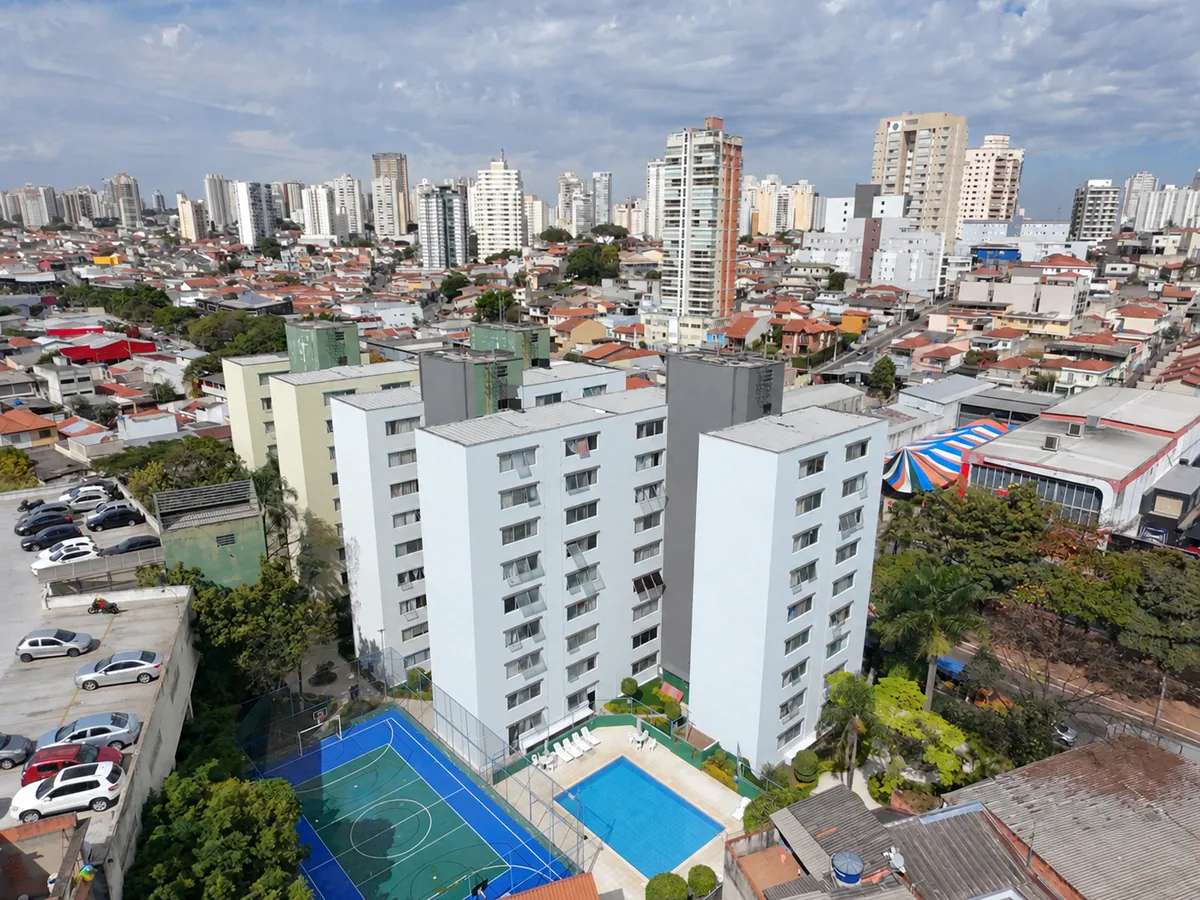 Vista aérea de condomínio com fachadas brancas e cinzas, quadra e piscina