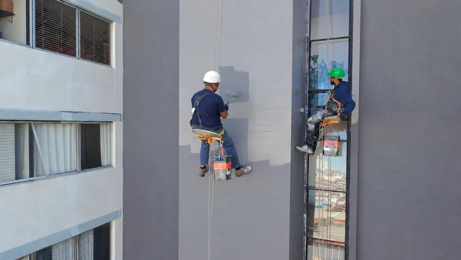 Profissionais em cadeiras suspensas realizando serviços na fachada do edifício